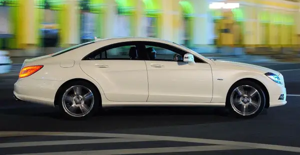 Biały Mercedes CLS 63 AMG mija nocą rozmyte światła miasta, jego sylwetka jest dynamiczna i elegancka.