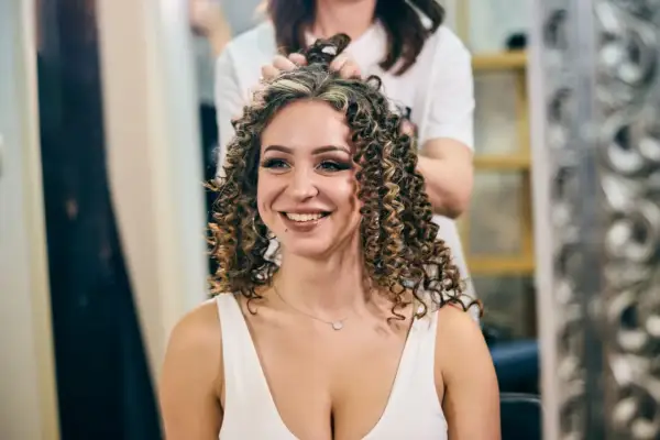 Une femme souriante se fait faire une permanente chez le coiffeur. Ses cheveux bouclés sont magnifiques.