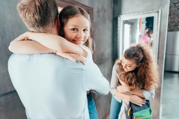 Dziewczynka mocno przytula tatę, jej uśmiech świadczy o dobrym samopoczuciu i zdrowej psychice. Mama tuli synka w tle.