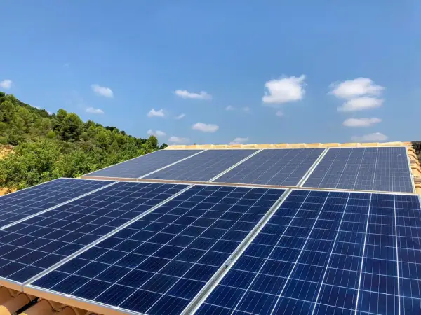 Mi experiencia con placas solares: paneles azules captan la luz del sol en un tejado, con colinas verdes y cielo azul de fondo.