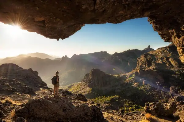 Una persona con mochila admira el paisaje montañoso al amanecer, disfrutando de unas increíbles caminatas Gran Canaria.