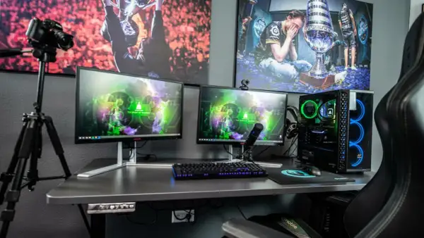 Ein Streamer-Setup: Zwei Monitore, Mikrofon, Kamera auf Stativ, Gaming-PC mit blauer Beleuchtung und Bilder von E-Sport-Erfolgen. So macht ein Streamer seine Inhalte.