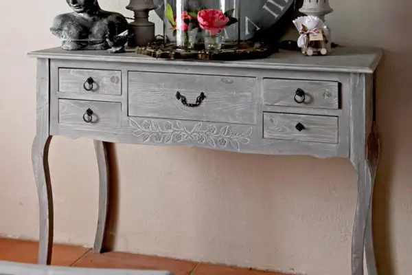 Console grise patinée, ornée de motifs floraux sculptés. Ce meuble à tiroirs, idéal pour un intérieur cosy, invite à y poser des objets décoratifs.