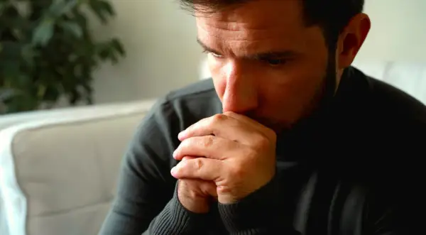 Man met handen voor zijn mond, diep in gedachten verzonken. Een blik van angst voor mannen, verborgen in zijn ogen.