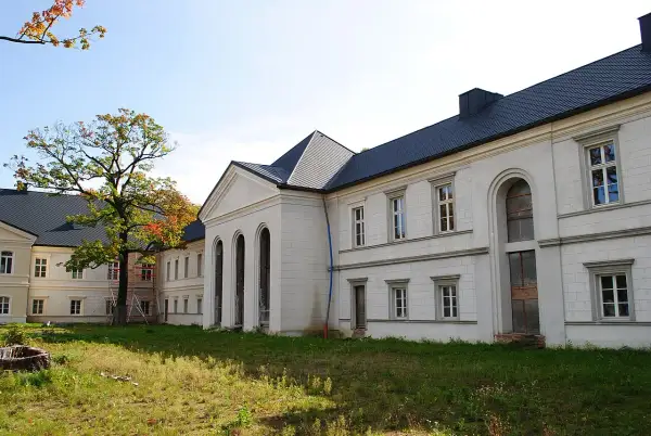 Pałac w Siemianowicach Śląskich, biała fasada z arkadowymi oknami i ciemnym dachem, otoczony zielenią i jesiennym drzewem.