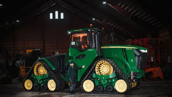Man bredvid en stor grön John Deere-traktor i en lada. Frågan "hur länge håller diesel" kan vara relevant för denna maskin.