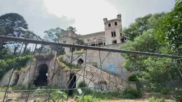 Ruines d'un château délabré, envahi par la végétation et couvert de graffitis. Un portail orné et des tours menacent de s'effondrer. Une scène d'urbex flippant.