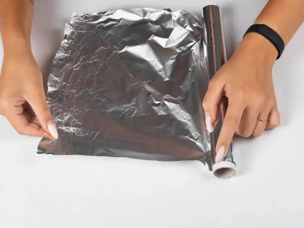 Dłonie rozwijają folię aluminiową, by zapobiec powstawaniu kożucha na sosie. Jak go zabezpieczyć folią?