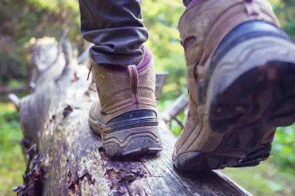 Osoba w butach trekkingowych stąpa po powalonym drzewie. Czy buty trekkingowe powinny być większe? Wygoda na szlaku jest kluczowa.