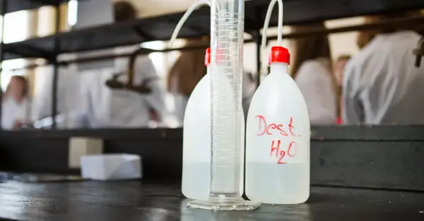 Bouteilles d'eau distillée et éprouvette graduée sur un établi de laboratoire, prêtes pour la stérilisation eau chaude.