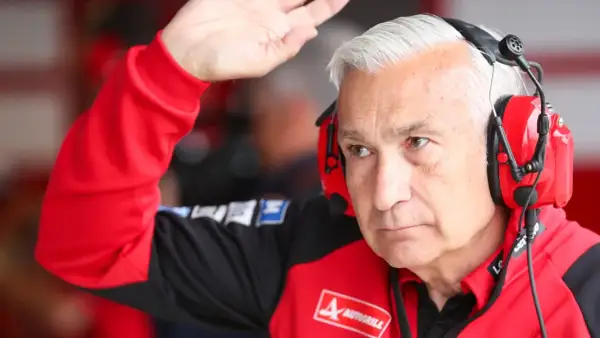 Davide Tardozzi, con auriculares rojos, saluda con la mano. Viste una chaqueta roja de equipo de carreras.