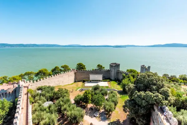 Vista dall'alto di un castello con un cinema all'aperto, circondato da ulivi e affacciato sul lago Trasimeno, uno dei borghi vicino Castiglione del Lago.
