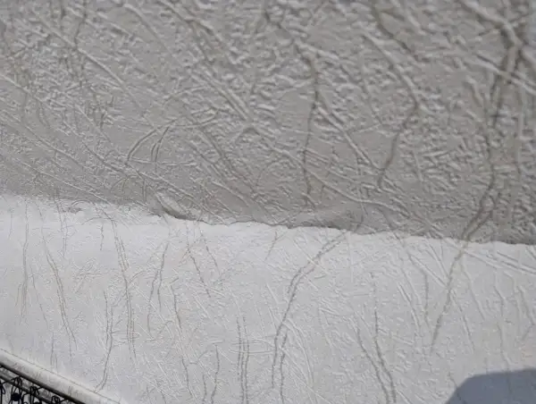 Detaljbild av vit, mönstrad tapet som täcker ett snedtak. Mönstret liknar kvistar eller ådring.