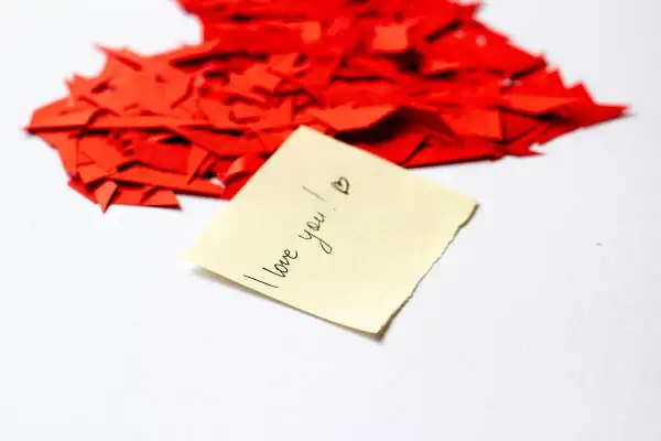 Serce z czerwonych skrawków papieru, a na nim karteczka z napisem "I love you!". Kocham Cię po polsku.