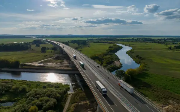 Most na Via Baltica przecina malowniczą dolinę rzeki, po której płyną ciężarówki.