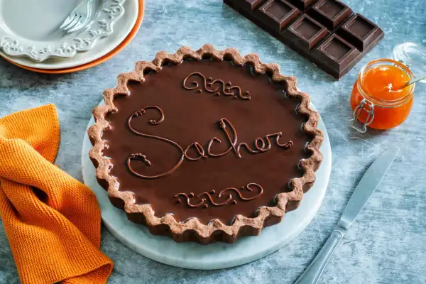 Una crostata Sacher lucida e invitante, con decorazioni in cioccolato e un vasetto di marmellata d'arancia accanto.