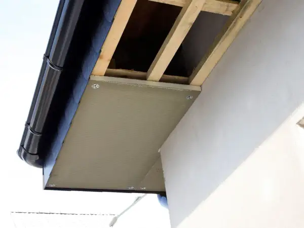 Montaż podprzybitki pod okapem dachu, widoczne drewniane krokwie i rynna.
