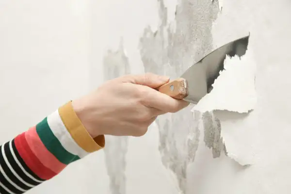Mano con spatola rimuove vernice vecchia scrostata, preparando il muro per un nuovo strato, forse antiruggine.