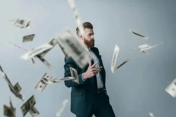 Mężczyzna w garniturze rzuca pieniędzmi, jakby świętował sukces swojego innowacyjnego patentu.