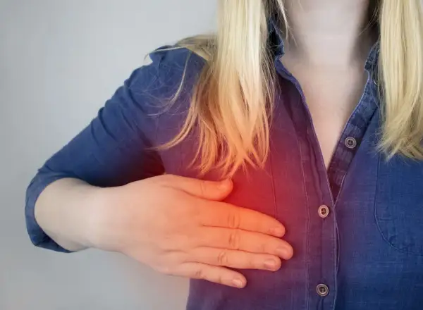 Kobieta z blond włosami dotyka piersi, gdzie widoczny jest czerwony obszar bólu, sugerujący potrzebę biopsji torbieli w piersiach.