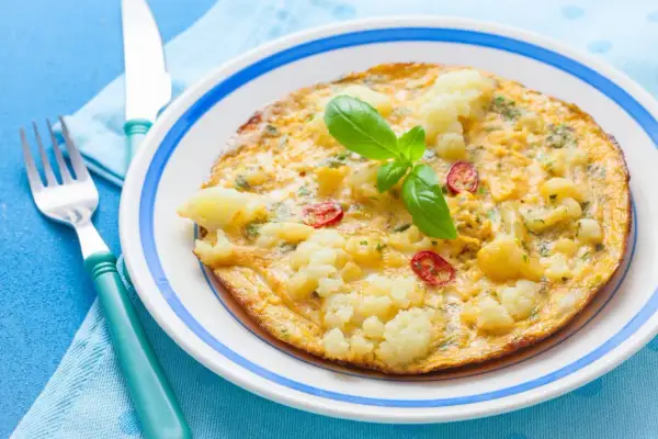 Omlet z kalafiorem i pomidorkami, idealny na lekki obiad. Udekorowany listkiem bazylii.