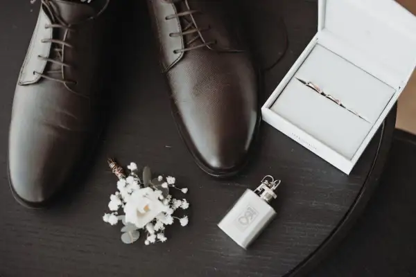 Eleganckie, brązowe oksfordy – jeden z klasycznych rodzajów butów męskich. Obok butonierka, obrączki i piersiówka.
