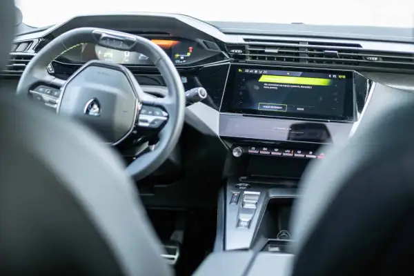 Nowoczesne wnętrze Peugeot 408 z cyfrowymi zegarami i ekranem dotykowym. Widoczny fragment kierownicy i konsoli środkowej.