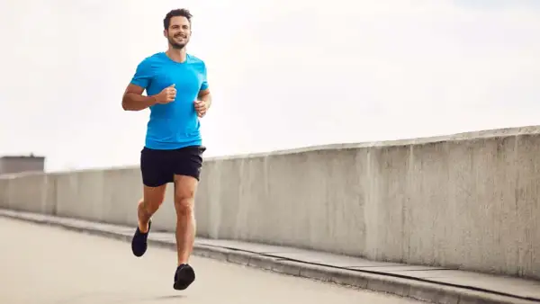 Lächelnder Mann joggt auf einer Straße, baut beim Joggen Muskeln auf.