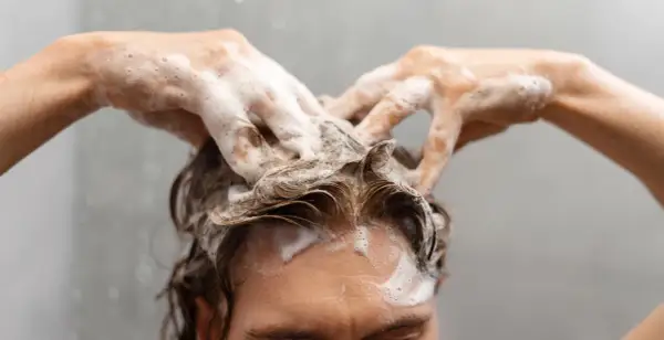 Manos con espuma masajean el cuero cabelludo, demostrando cómo lavarse el pelo correctamente para una limpieza profunda y un cabello saludable.