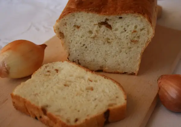 Pyszny chleb cebulowy na drożdżach, świeżo upieczony, z widocznymi kawałkami cebuli w miękiszu. Obok leżą całe cebule.