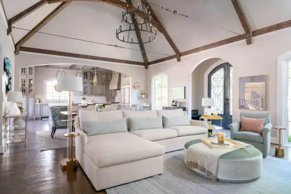 A spacious living room with a sectional sofa, armchair, and ottoman. The vaulted ceiling with exposed beams and a large chandelier create a dramatic focal point, showcasing what is the best way to arrange furniture for an open, airy feel.