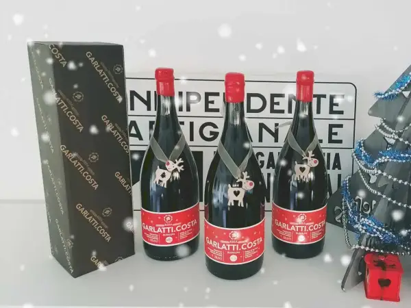 Tre bottiglie di birra Garlatti.Costa con decorazioni natalizie, una scatola e un albero di Natale sullo sfondo.
