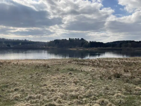 Ein ruhiger Blick auf den Krombachtalsperre Rundweg mit bewaldeten Ufern und einem Himmel voller Wolken.