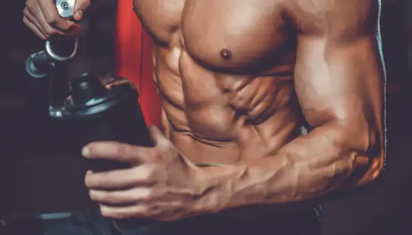 Atleta con addominali scolpiti prepara un frullato, mostrando a cosa servono le proteine in polvere palestra per la crescita muscolare.