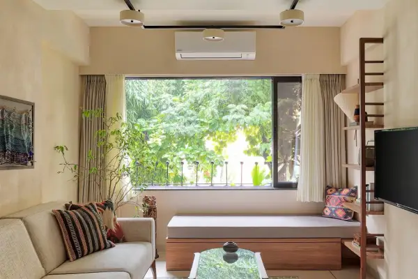 Cozy living room with a large window overlooking lush greenery, a comfortable sofa, and a built-in bench, making this small house feel spacious.
