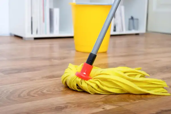 Ein gelber Wischmopp liegt auf einem Holzfußboden, bereit, den Boden zu wischen. Ein gelber Eimer steht im Hintergrund.