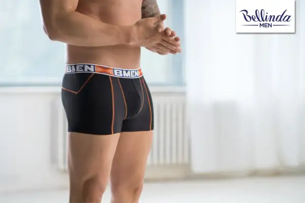 Mężczyzna w czarnych bokserkach z pomarańczowymi szwami i logo marki. Wybór między slipami a bokserkami to kwestia komfortu.