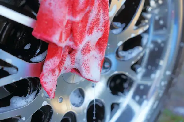 Un chiffon rouge savonneux nettoie une jante de voiture brillante. Un nettoyant jantes maison efficace pour un résultat impeccable.