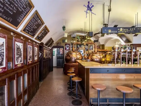 Interno di un locale tradizionale con alambicchi di rame, sgabelli e insegne che richiamano il mondo della birra e del **hopfen & co.**