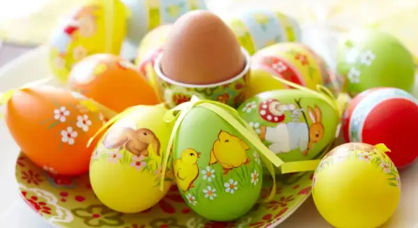 Un assortimento di colorate decorazioni uova di Pasqua con coniglietti, pulcini e fiori. Un uovo marrone è in un portauovo decorato.