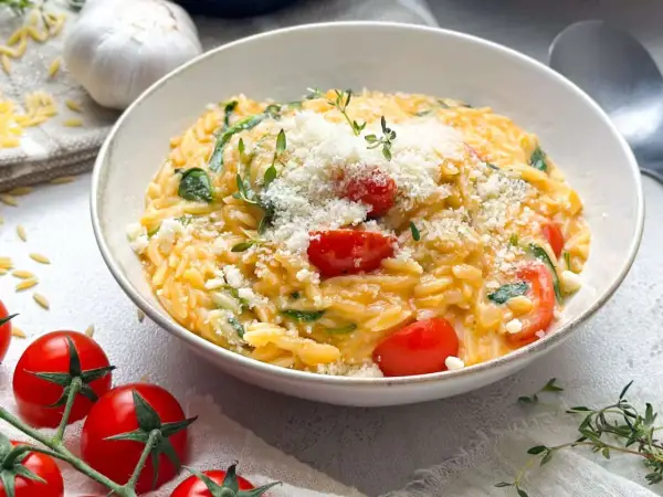 Schüssel mit Orzotto, Tomaten, Spinat und Parmesan, garniert mit Thymian.