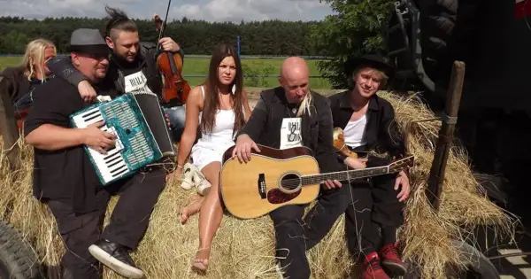 Zespół muzyczny siedzi na sianie, grając na akordeonie, skrzypcach i gitarze. Ich muzyka to hołd dla Ukrainy, śpiewają podaj rękę Ukrainie.