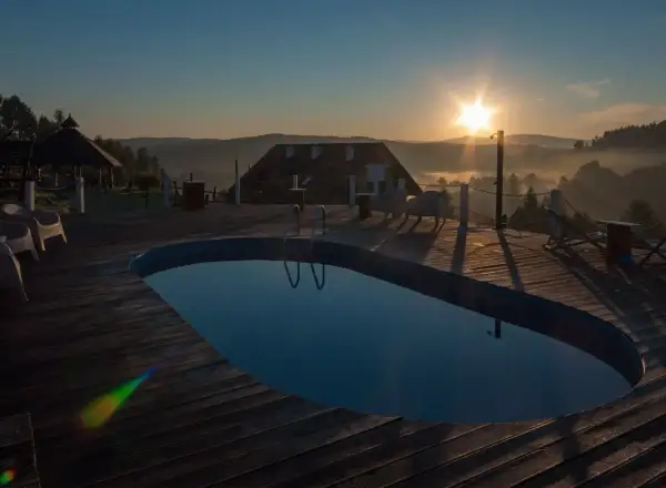 Poranek nad basenem z widokiem na Bieszczady. Słońce wschodzi nad mglistymi dolinami, tworząc magiczną atmosferę. Idealne miejsce na relaks w **termy Bieszczady**.