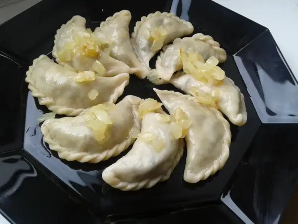 Pyszne pierogi z płuckami, polane skarmelizowaną cebulką, kuszą na czarnym talerzu.