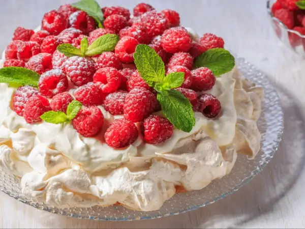 Beza Pavlova, która zawsze wychodzi, udekorowana świeżymi malinami i listkami mięty, posypana cukrem pudrem.