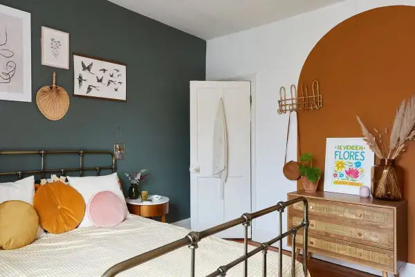 A cozy bedroom with a dark green accent wall, white door, and a terracotta arch. This space shows how to make a small bedroom look bigger with light bedding and strategic decor.