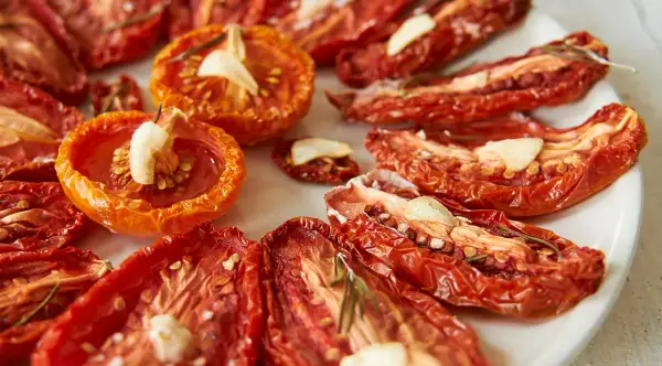 Getrocknete Tomaten mit Knoblauch und Rosmarin auf einem Teller.