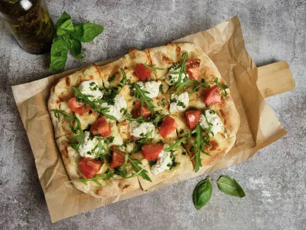 Pyszna pizza z pomidorami, mozzarellą i rukolą. Idealna inspiracja, z czym zrobić pizzę na szybki obiad.