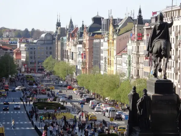 Pomnik konny na placu Wacława w Pradze, z widokiem na tętniącą życiem ulicę pełną ludzi i samochodów.