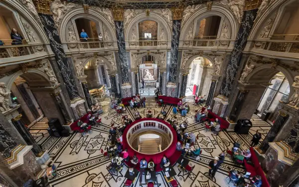 Wnętrze muzeum historii sztuki w Wiedniu z ludźmi przy stolikach i rzeźbą w centrum.